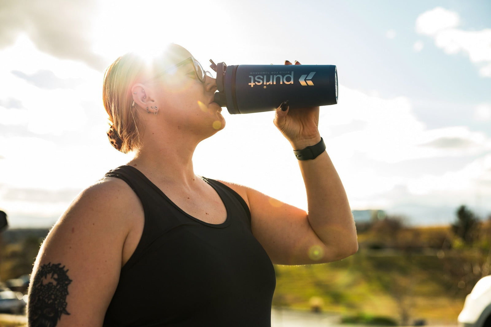 An athlete drinks from a shaker bottle as the sun shines behind her