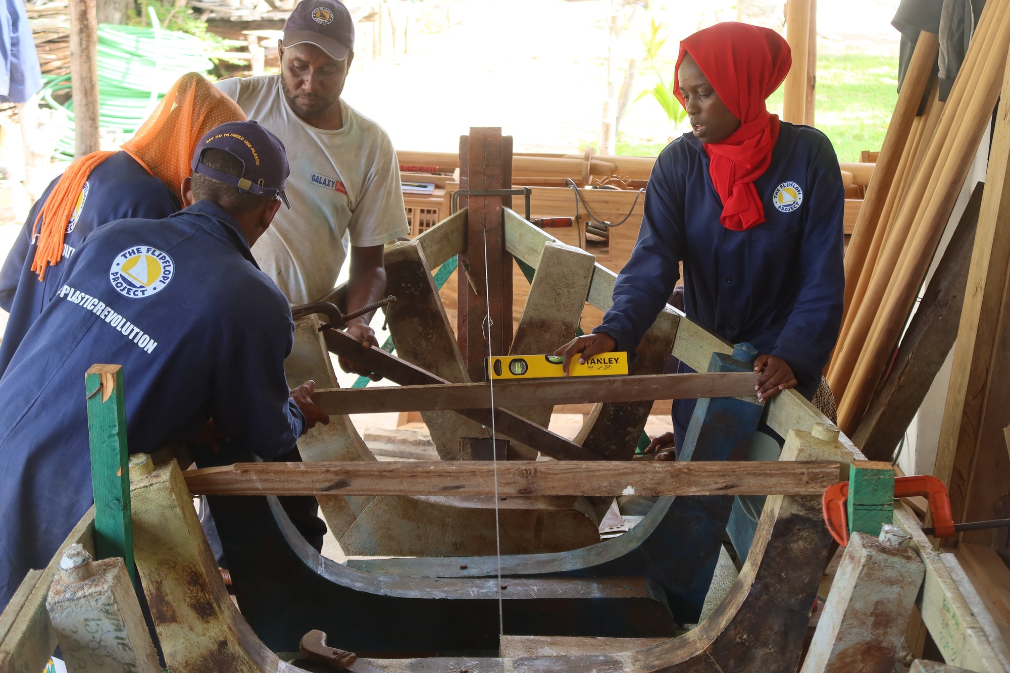 Three people working on a wooden boat in a workshop.